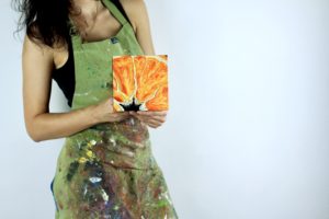 Angela Faustina holding her oil painting Orange IV, 2017. Oil on cradled painting panel, 6" by 6”.